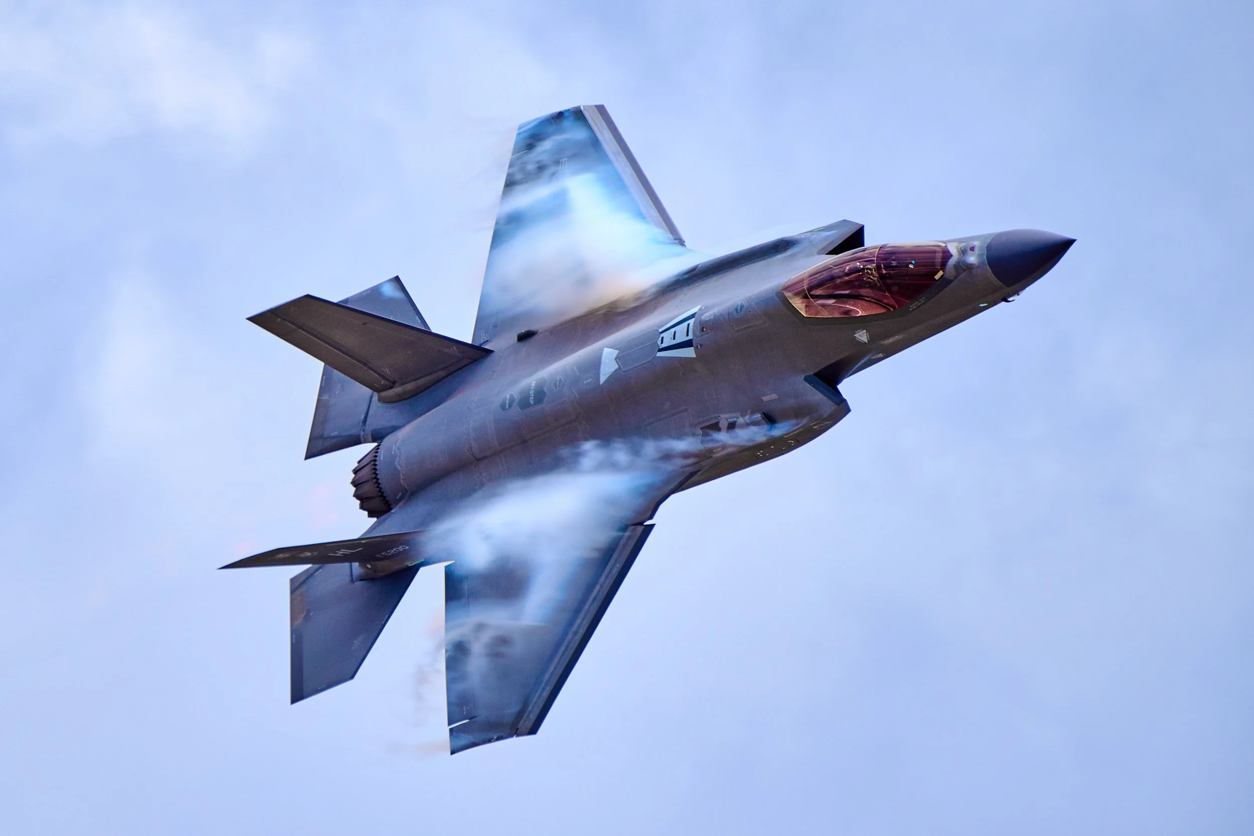 A fighter jet flying through the sky, emitting vapor trails behind it.