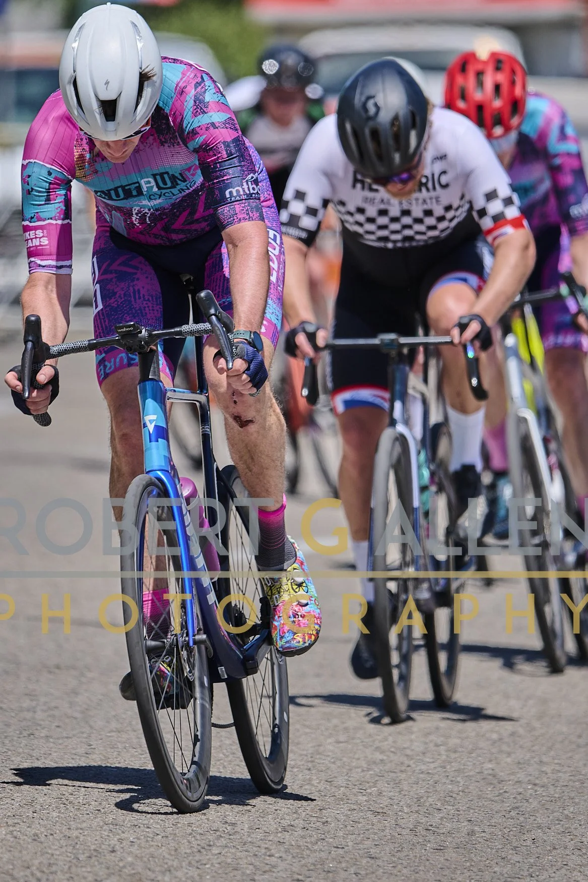 Cyclists wearing helmets and colorful cycling jerseys participating in a race, riding on a paved road.