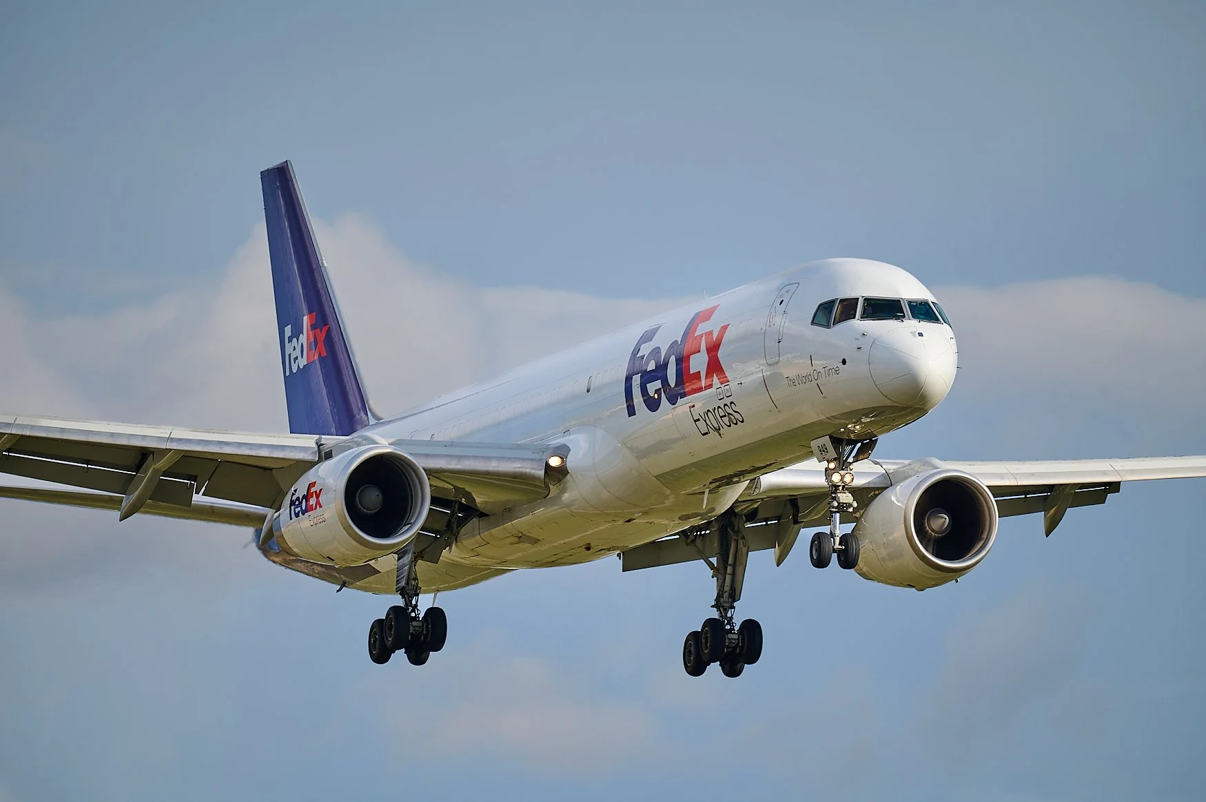A FedEx Express cargo airplane is flying in the sky with its landing gear extended.