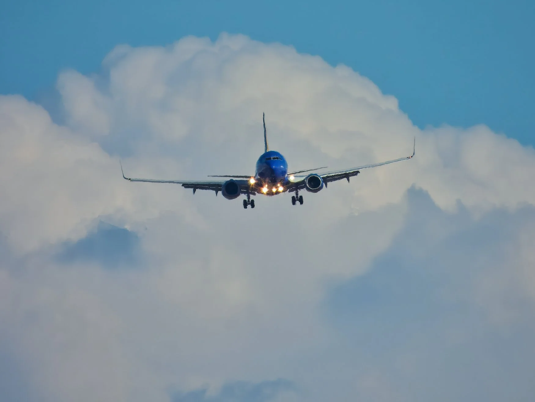 A blue commercial airplane flying through the sky with clouds in the background.