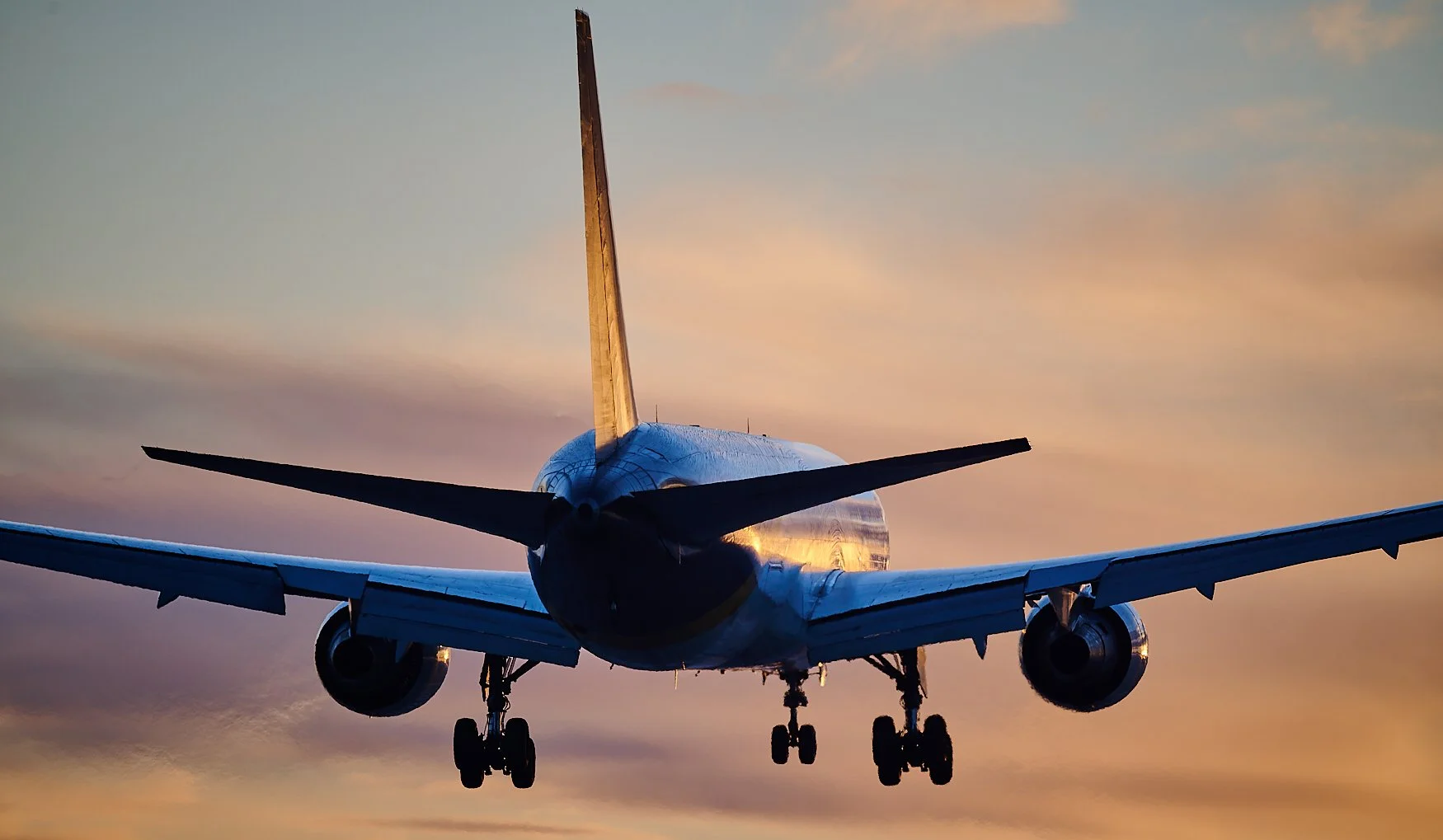 Rear view of a commercial airplane in flight during sunset, flying against a colorful sky with sunset hues.