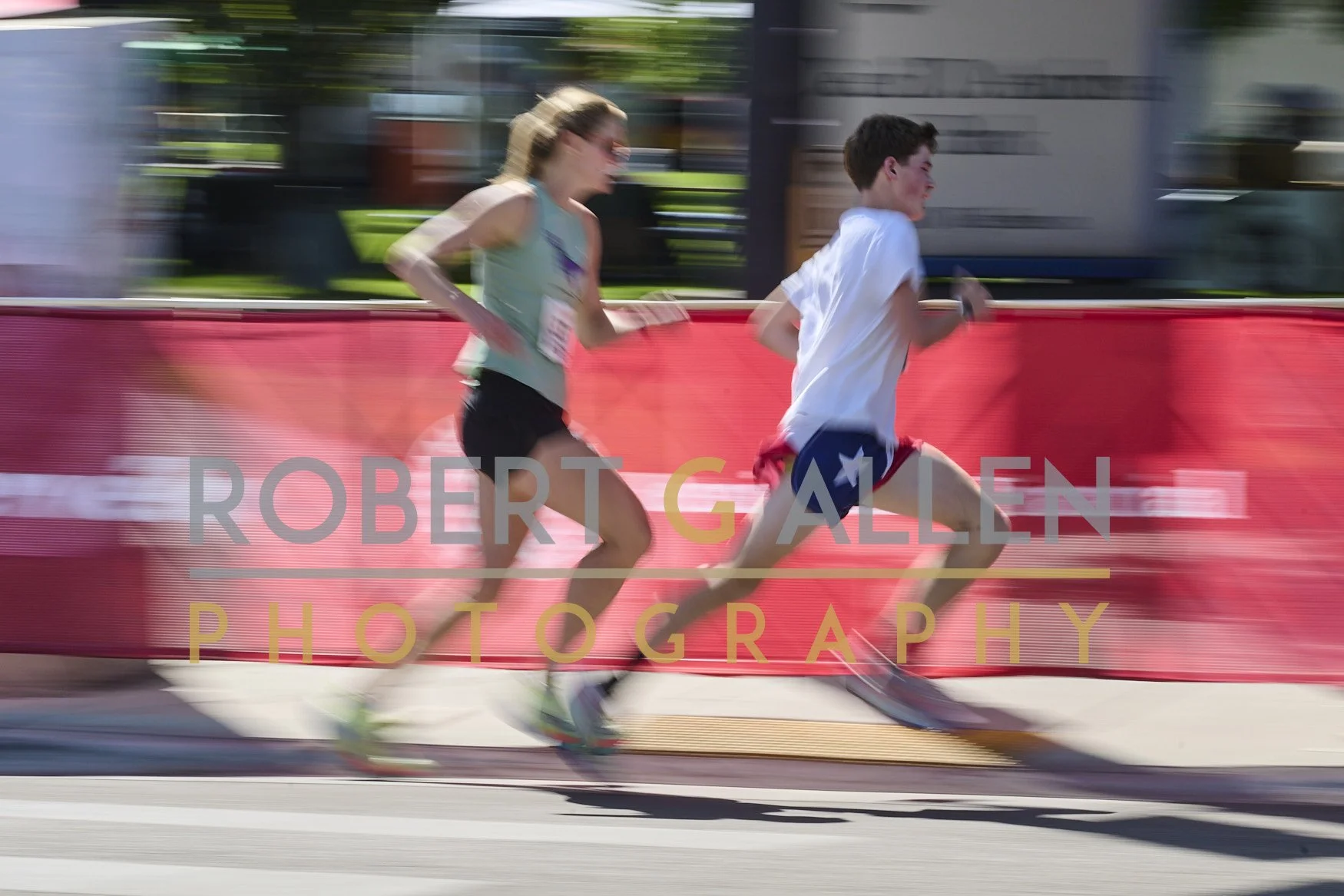 Two runners, a woman and a young boy, competing in a race along a city street, with motion blur indicating speed.
