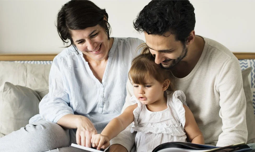 Parents reading with their young child on the couch at home