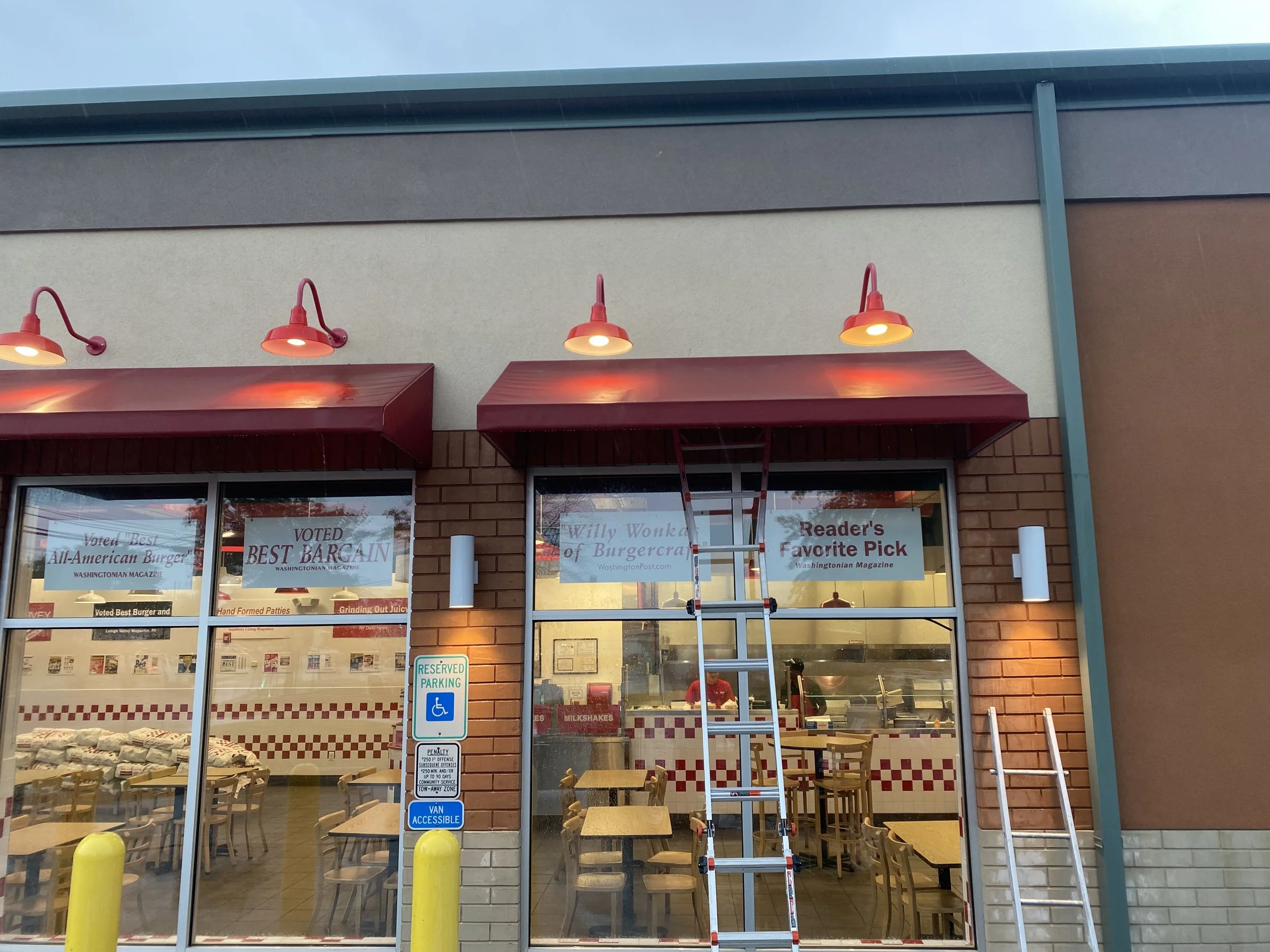 Front of a Burger King restaurant with red awnings, outdoor seating, and a ladder leaning against the building. Signs in the windows indicate awards and reader's favorite.