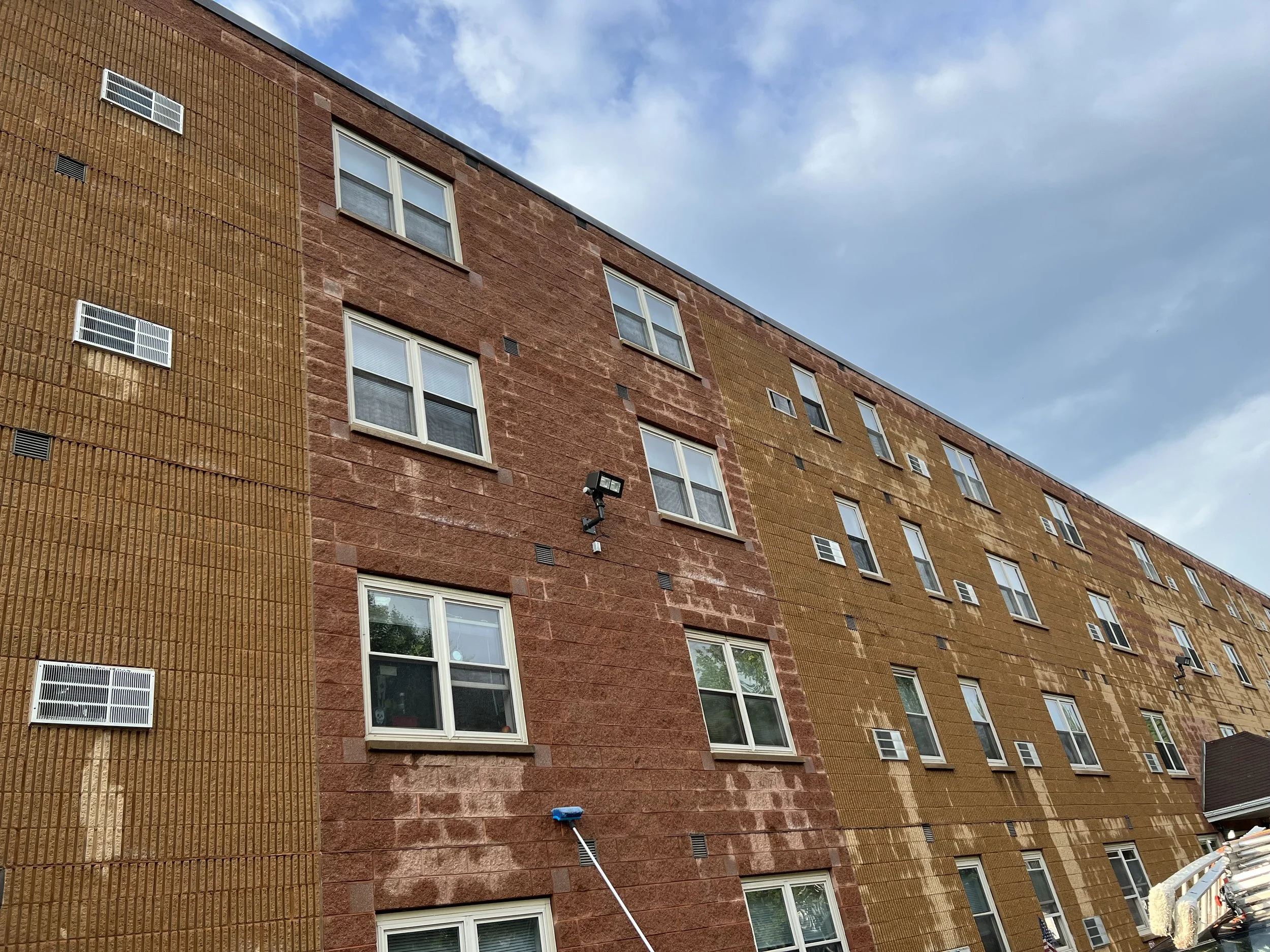 Multi-story residential building with brick exterior, multiple windows, and outdoor lighting, under a partly cloudy sky.