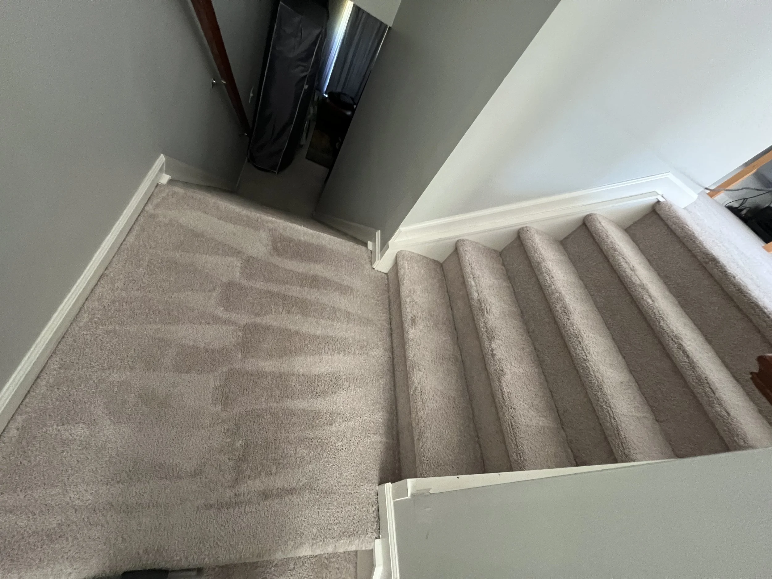 Staircase with beige carpet and a small beige carpeted landing at the top, leading to a dark-colored door.