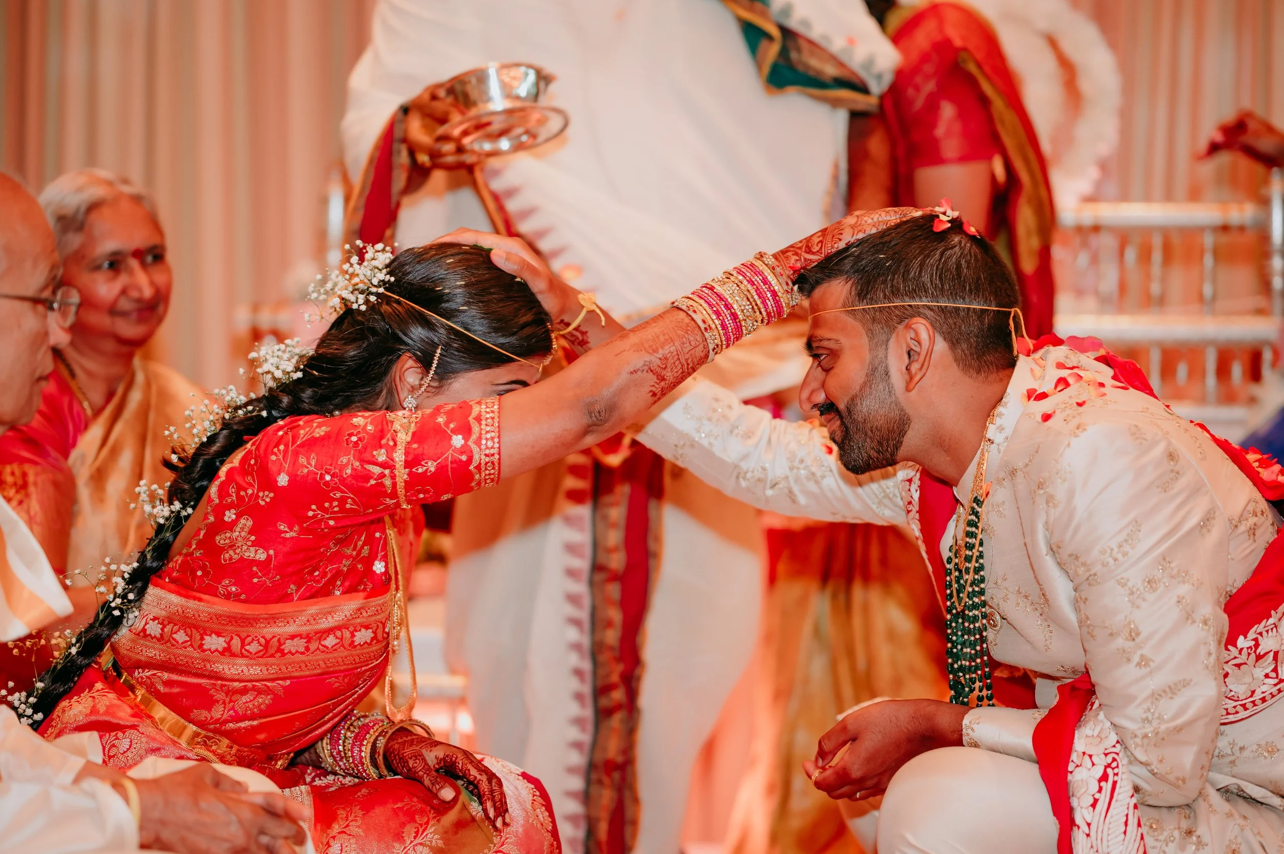Indian bride and groom performing a traditional wedding ritual with the bride touching the groom's forehead during their wedding ceremony.