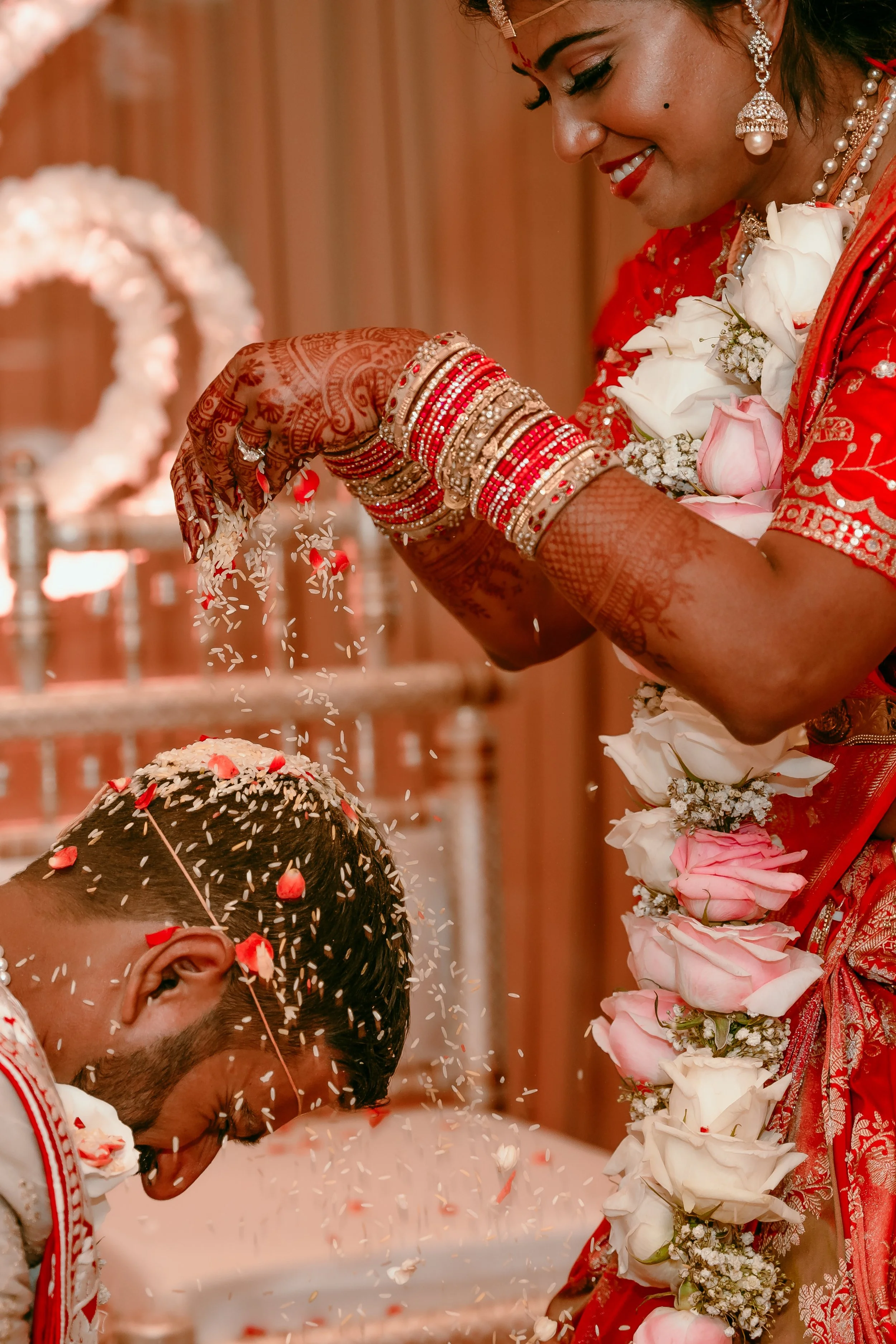 An Indian bride sprinkling flower petals over her groom's head during a traditional wedding ceremony.
