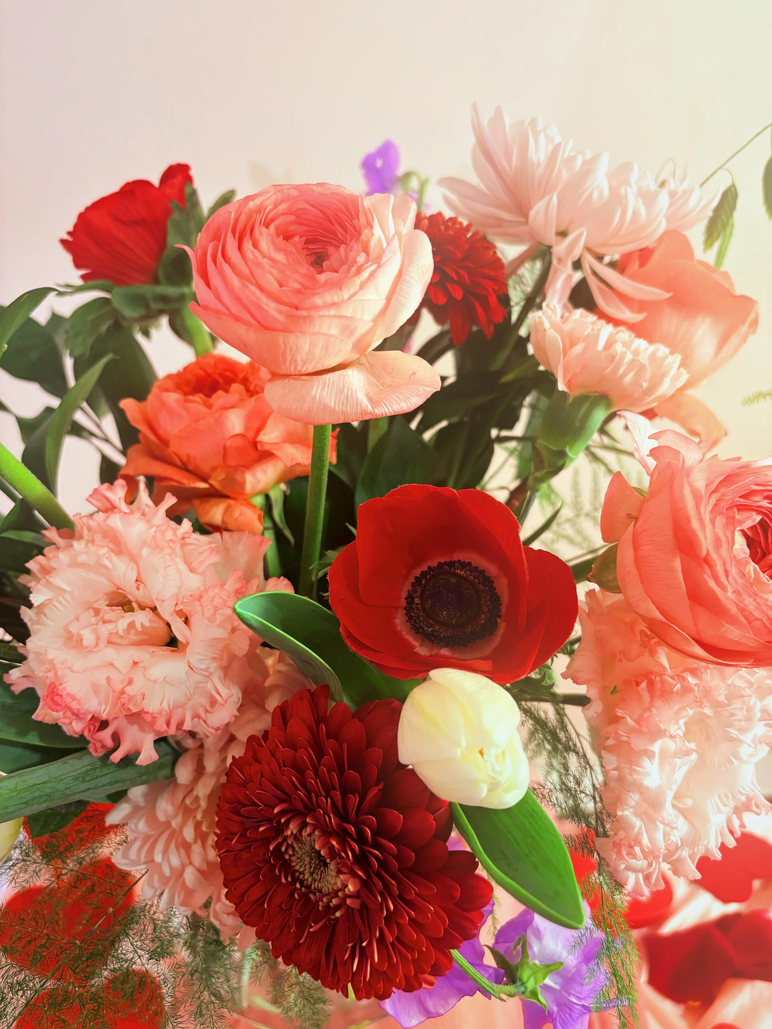 A colorful bouquet of various flowers including red, pink, peach, white, and purple flowers with green leaves.