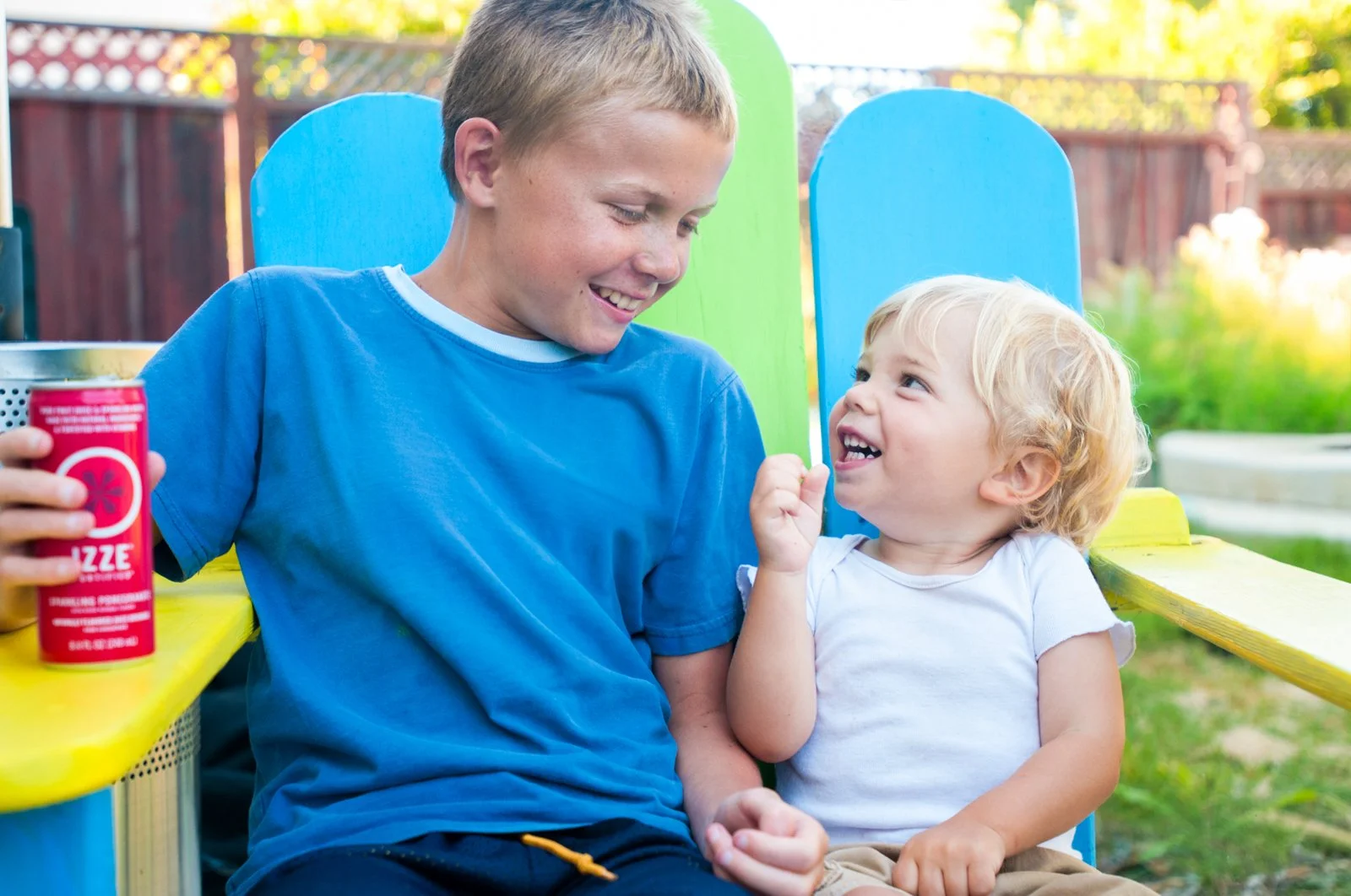 Two kids sitting on colorful benches outdoors, smiling and playing together during daytime.