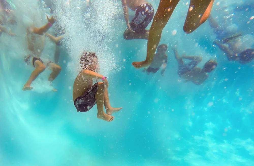 Children playing and diving underwater in a swimming pool.