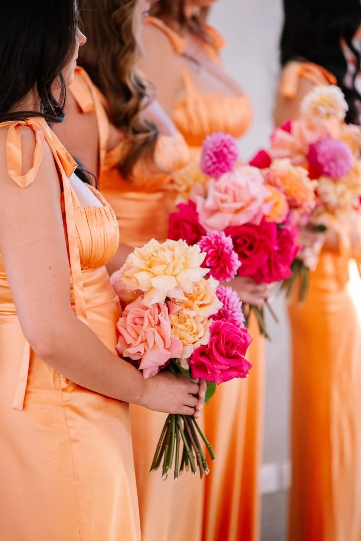 Bridesmaids in peach dresses holding pink, peach, and cream bouquets.