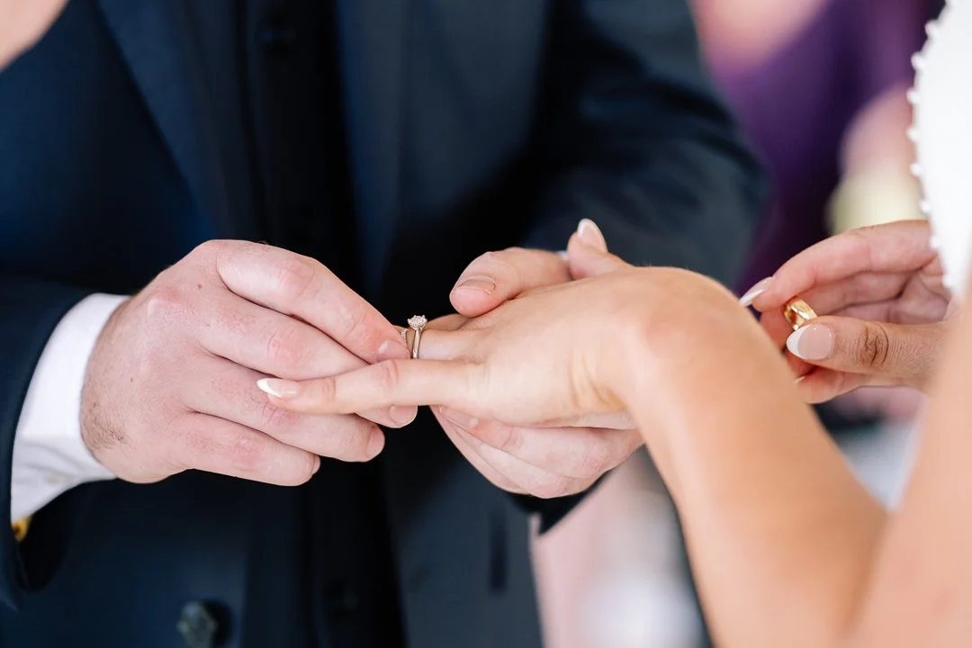 A person is placing a wedding ring on another person's finger during a wedding ceremony.