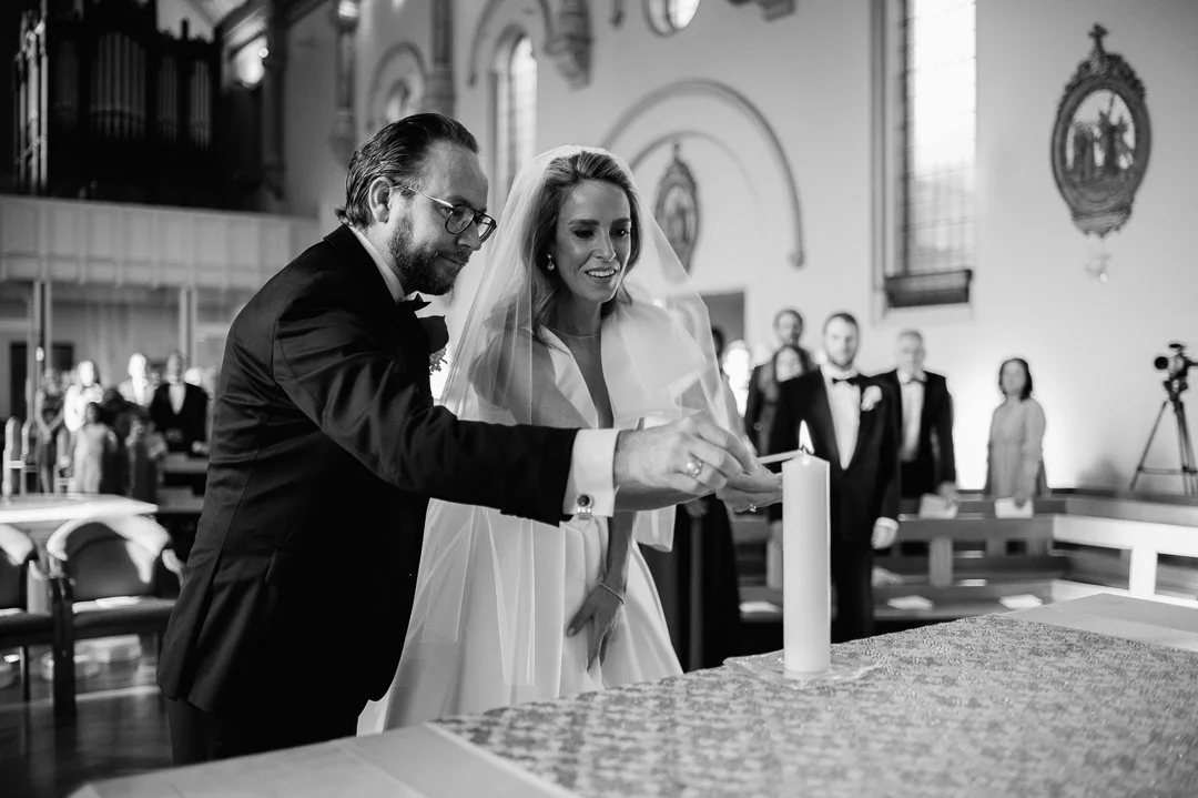 A bride and groom lighting a unity candle during their wedding ceremony in a church.