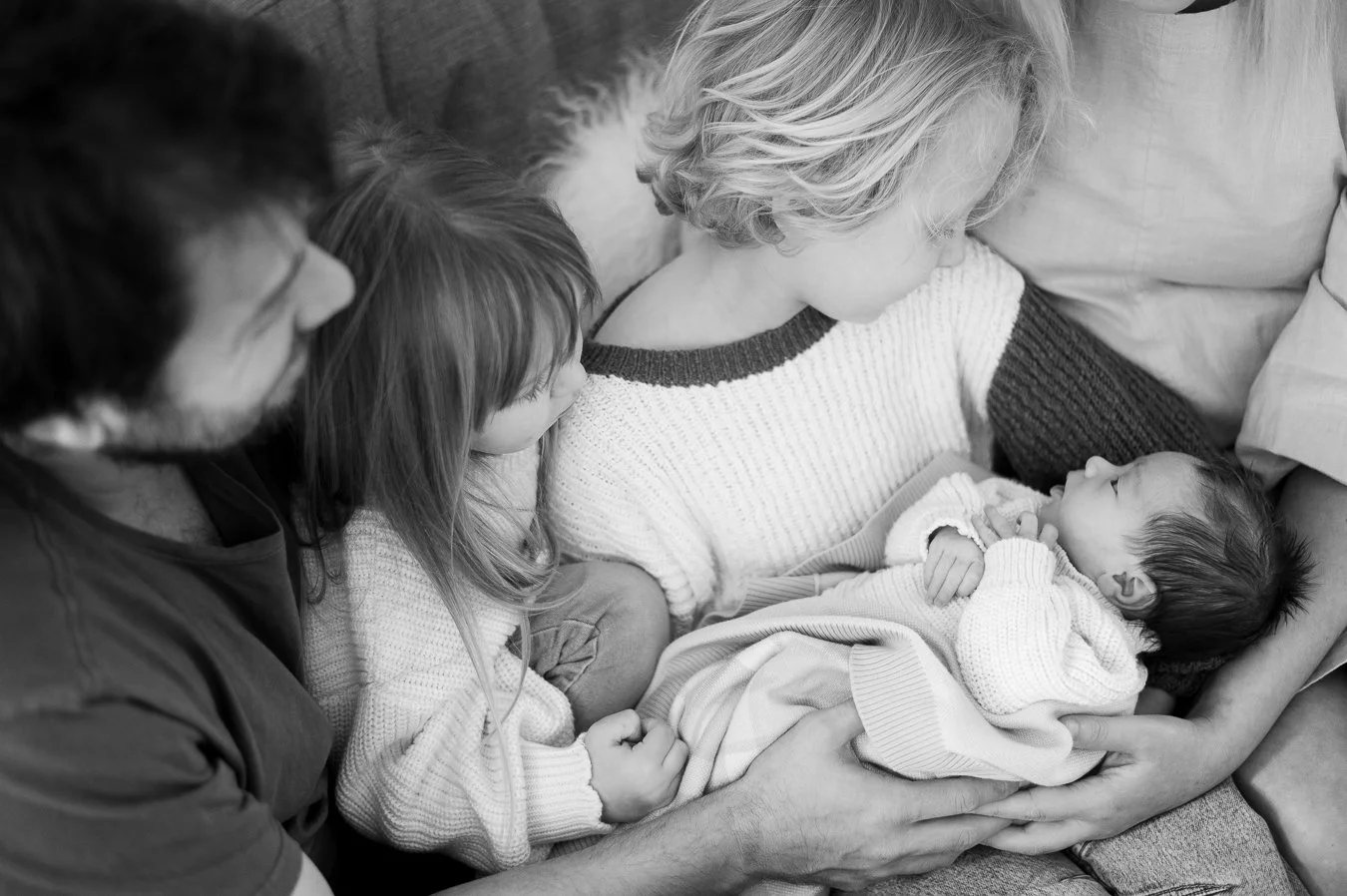 Family gathered around a newborn baby, with the mother holding the baby while the father and two children look on affectionately.
