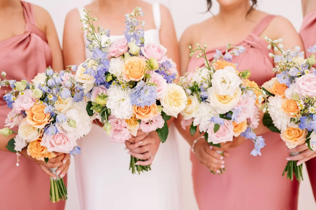 Group of women in pink dresses holding colorful flower bouquets at a wedding.