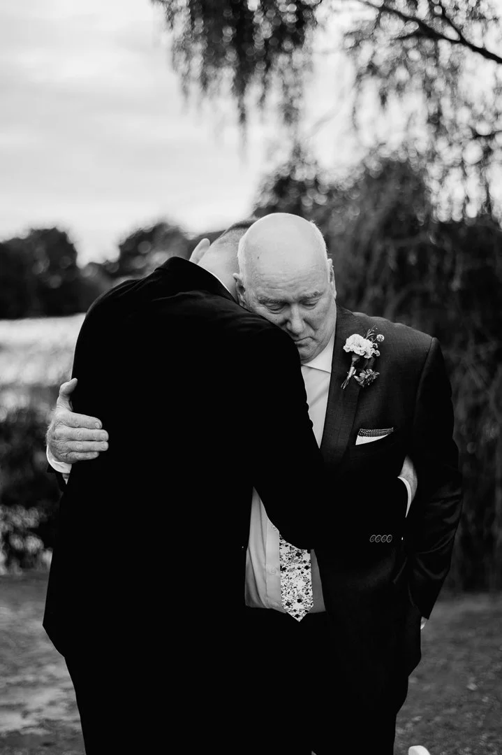 Two men in suits hugging outdoors, black and white photo.