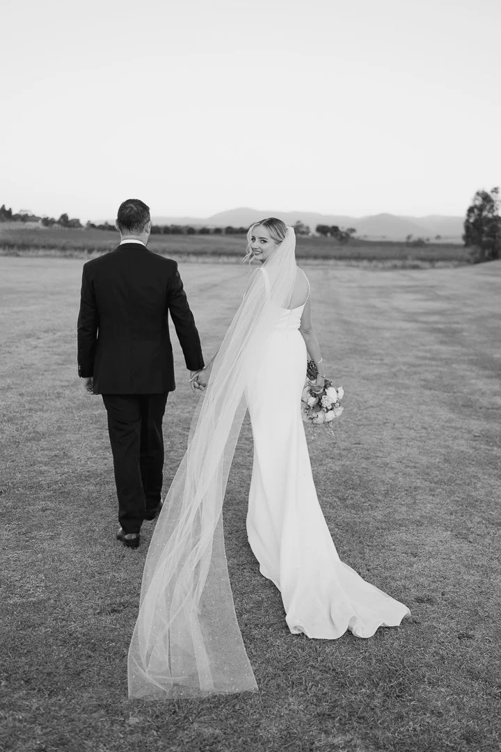 A bride and groom holding hands and walking away in an open field during a wedding.