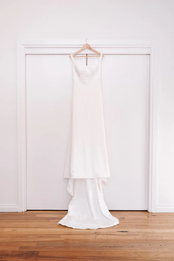 A white wedding dress hanging on a hanger against a white door in a room with wooden flooring.
