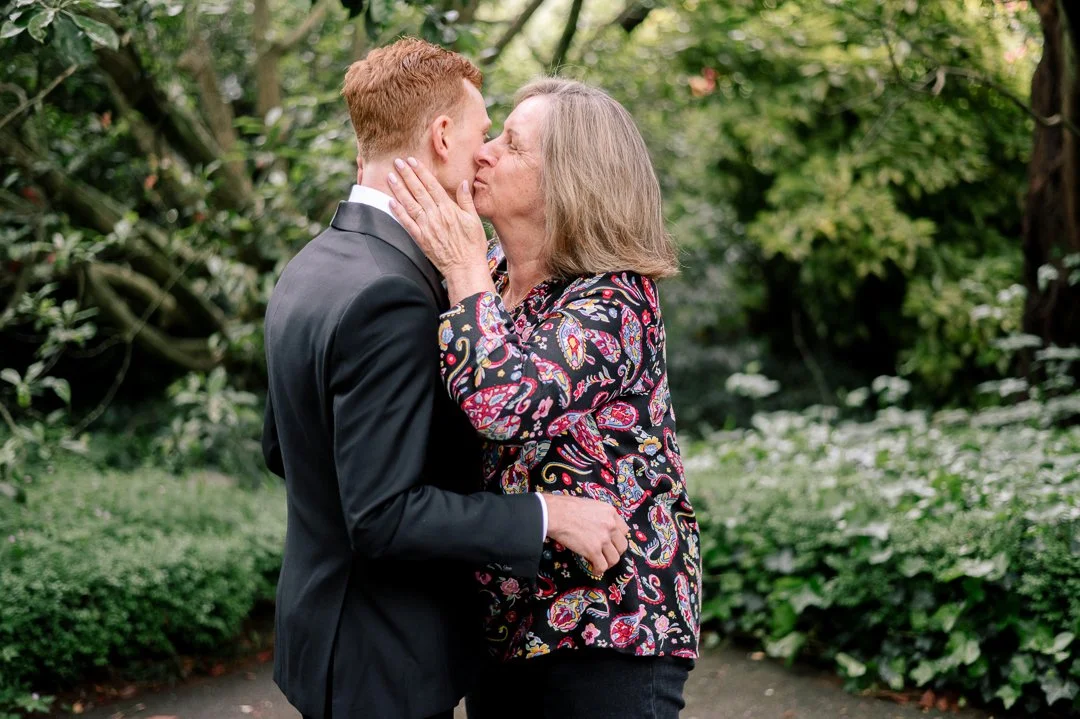 A woman and a young man share a kiss in a lush, green outdoor garden.