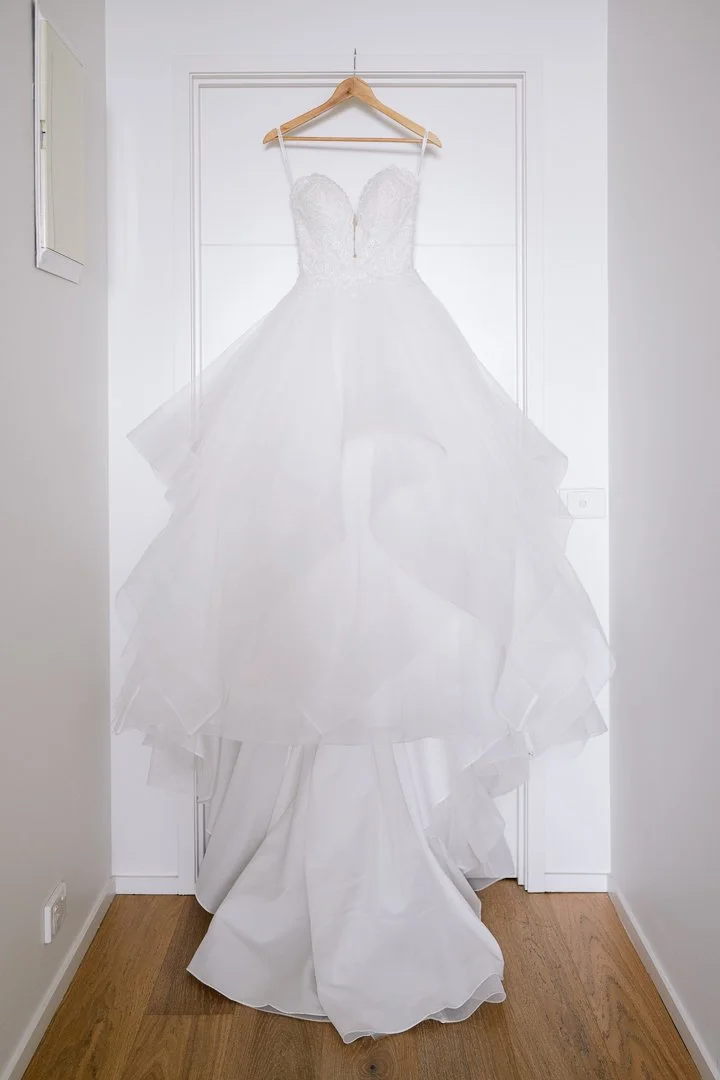 White wedding dress hanging on a wooden hanger against a white door.