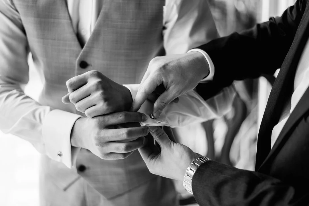 Close-up of multiple hands fastening a ring on a person's finger during a wedding ceremony, in black and white.