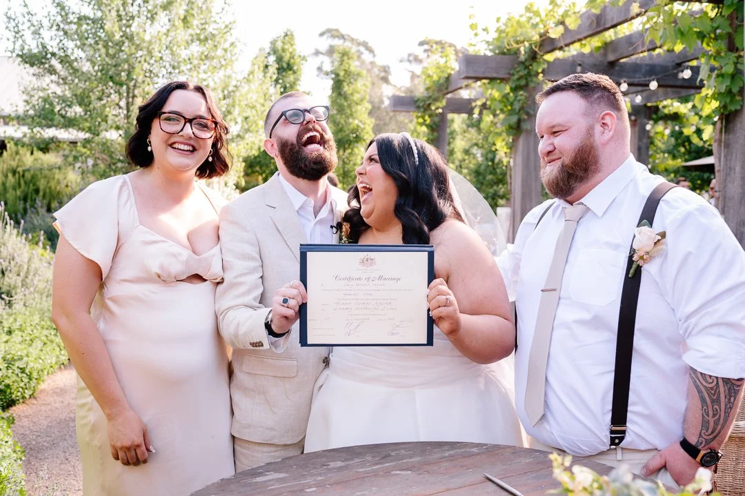 Group of people celebrating at a wedding outdoors, with one person holding a marriage certificate and all smiling and laughing.