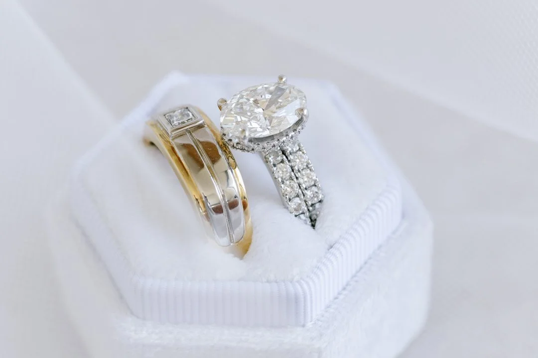 Close-up of two wedding rings, one with a large diamond and smaller diamonds, placed in a white jewelry box.