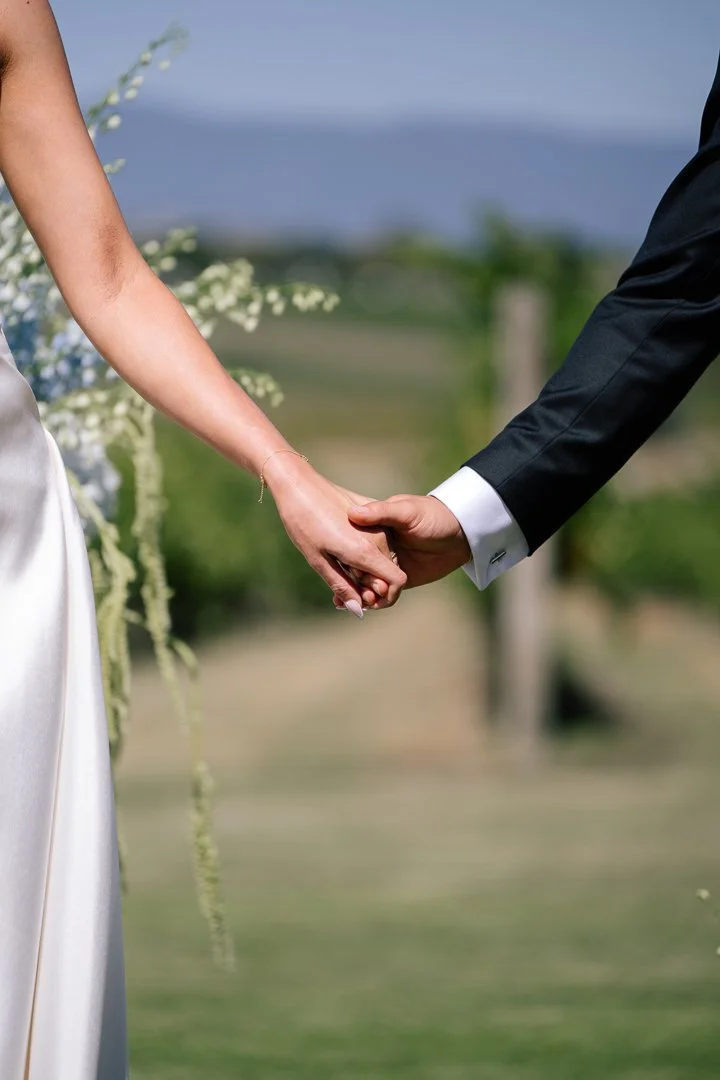 A bride and groom holding hands during a wedding ceremony outdoors.