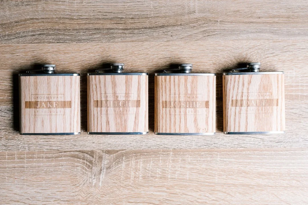 Four wooden flask bottles with engraved labels, placed on a wooden surface.