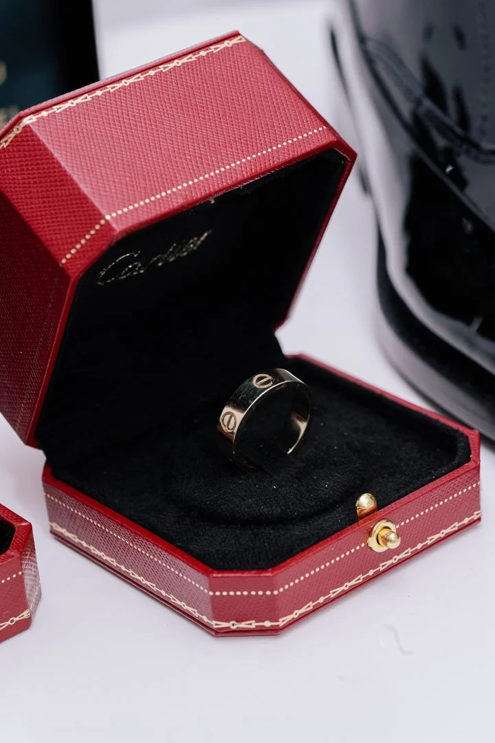 A black ring with a gold logo inside a black velvet jewelry box inside a red case, placed on a white surface.