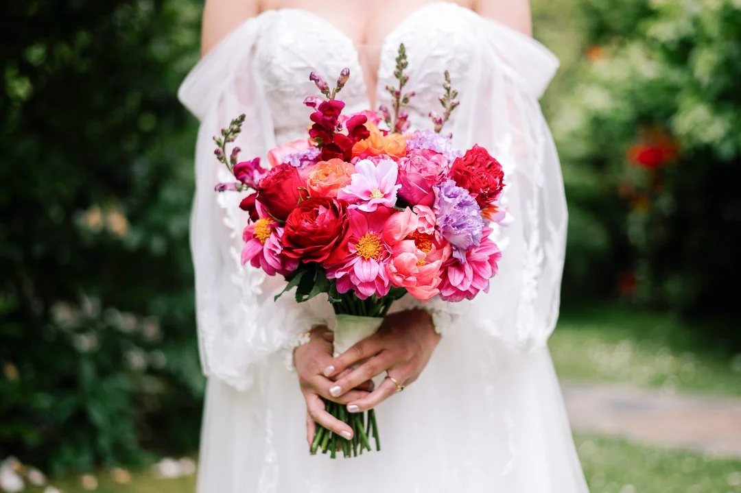 Person in a white dress holding a colorful bouquet of flowers outdoors.