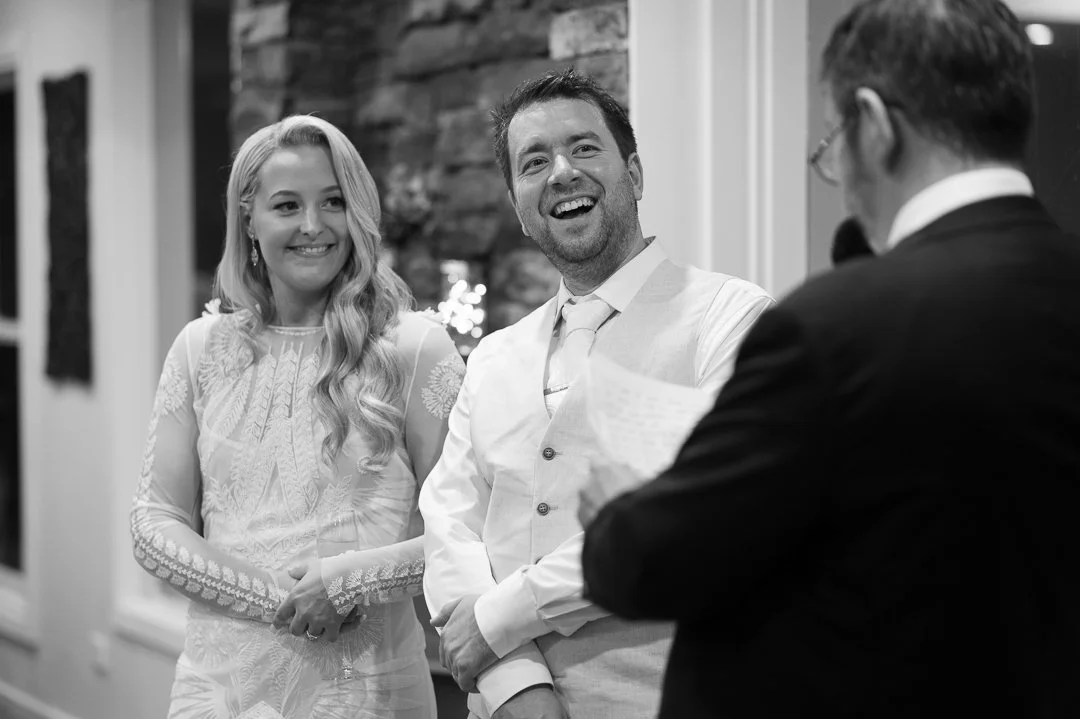 Three people standing together at a formal event, smiling and looking at each other, with a brick wall in the background.