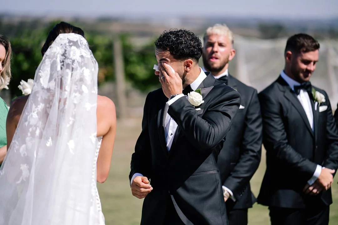 A groom in a black tuxedo crying during his wedding ceremony.