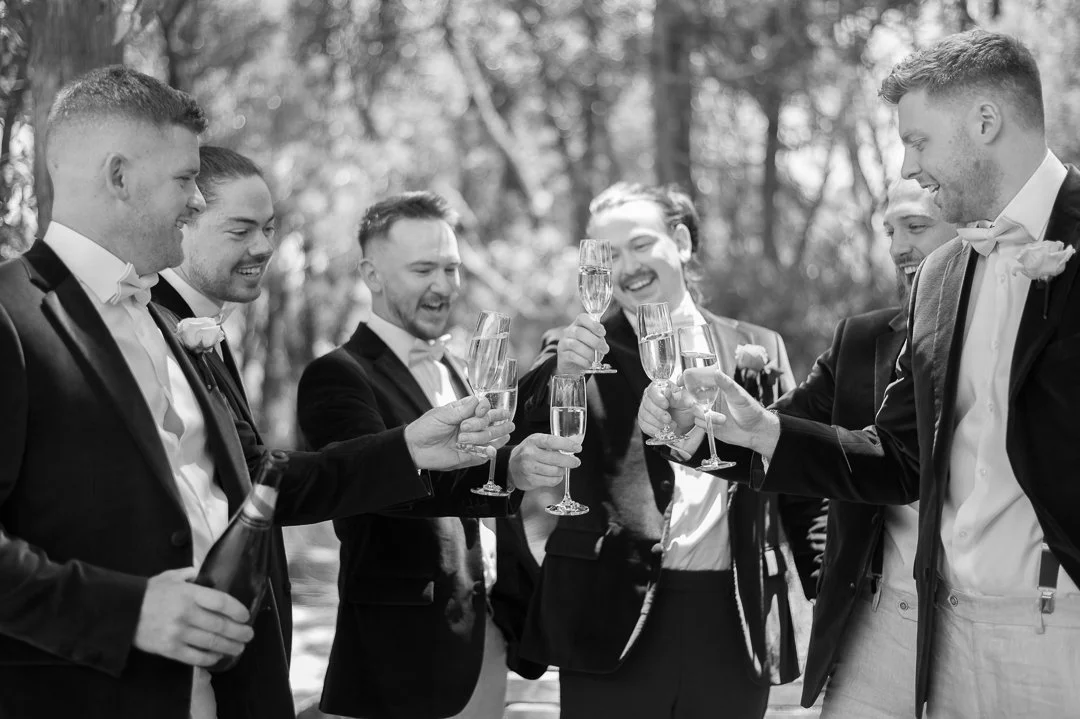 Group of men in tuxedos celebrating with champagne outdoors