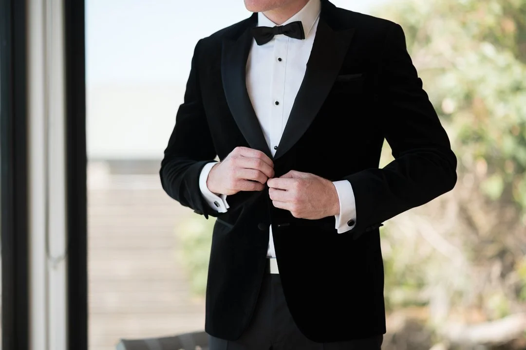 Man in black tuxedo adjusting his jacket with a bow tie.