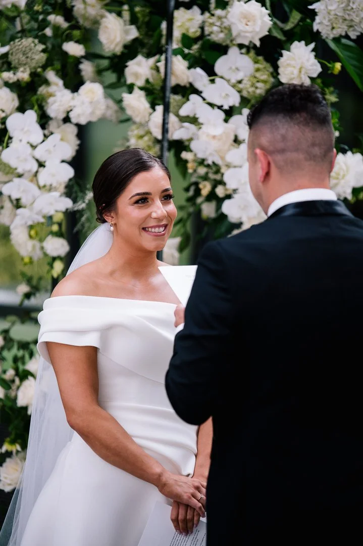 Bride and groom exchange vows at their wedding ceremony with a floral backdrop.