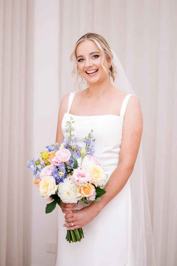 A smiling bride in a white wedding dress holding a colorful bouquet of flowers.