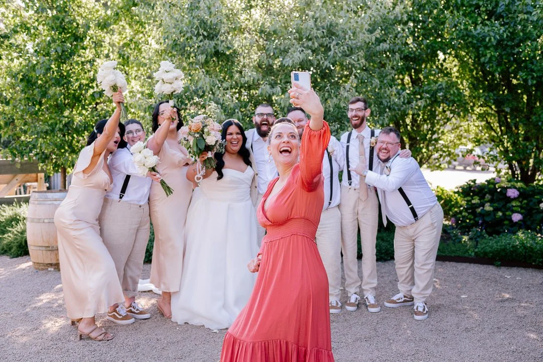 A group of people celebrating a wedding outdoors, taking a selfie together.