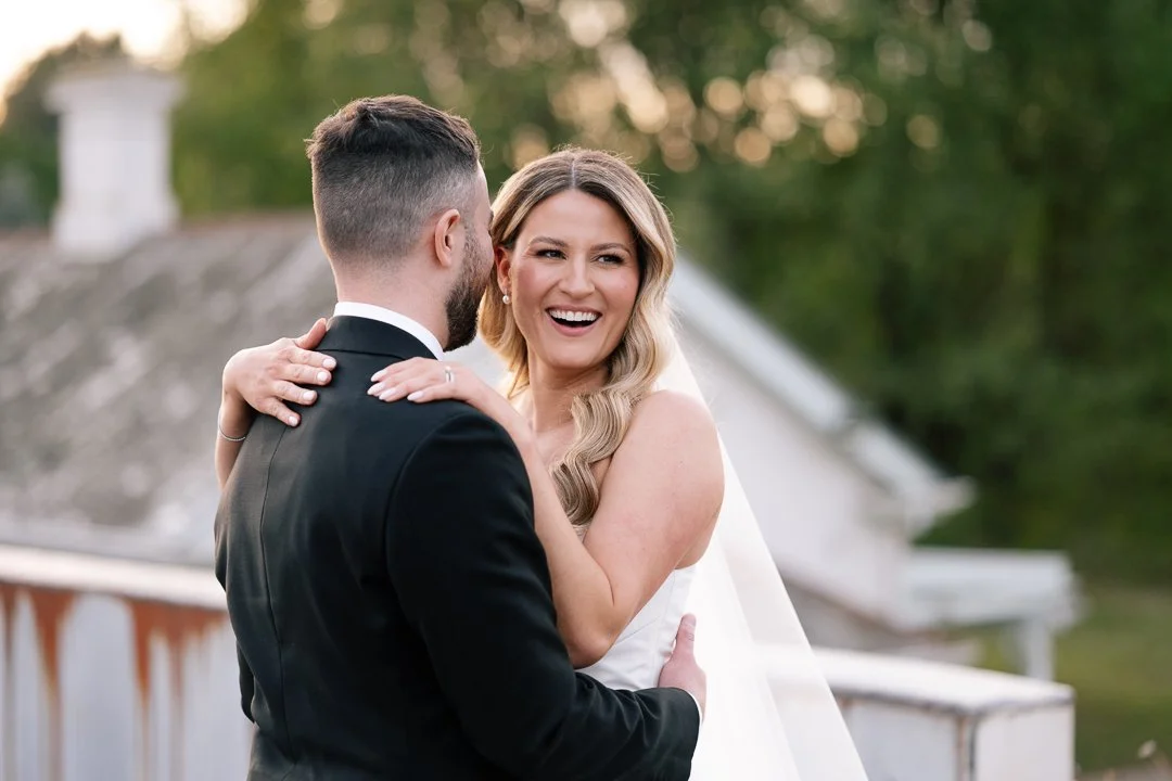 A bride and groom share a joyful moment outdoors on their wedding day, embracing and smiling.
