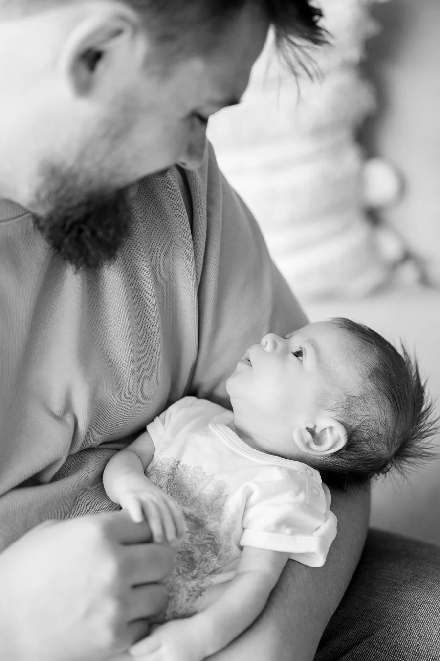 A man holding a baby in his arms, looking at the baby with affection, in a close-up black and white photo.