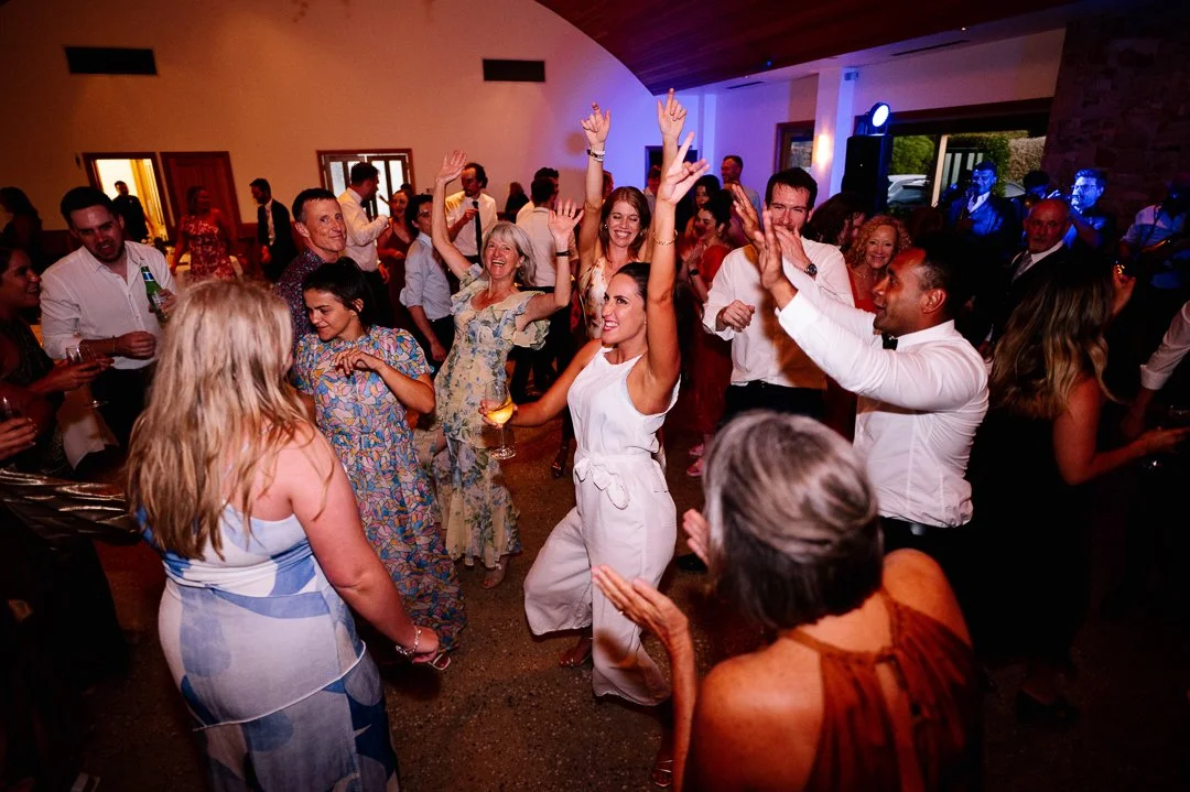 People dancing and celebrating at a party or wedding reception with colorful lighting and lively atmosphere.