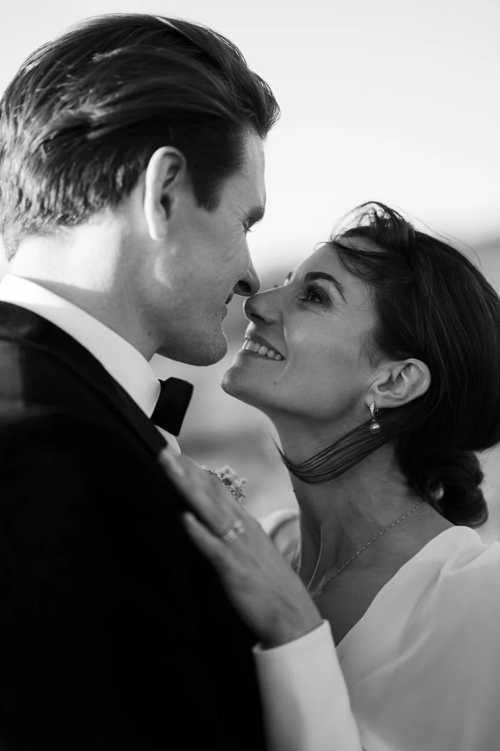 A black and white photo of a couple in a romantic moment, facing each other closely with smiles, dressed in formal attire.