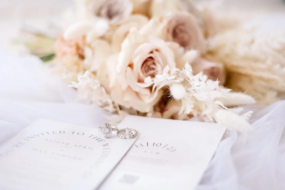 Wedding invitation with two rings and a bridal bouquet of white and blush roses and dried flowers