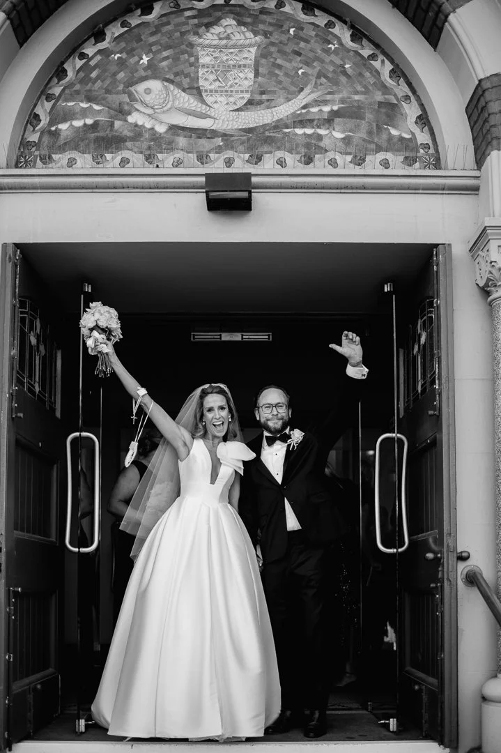 Bride and groom celebrating wedding exit at church entrance, with the bride holding a bouquet and both smiling.