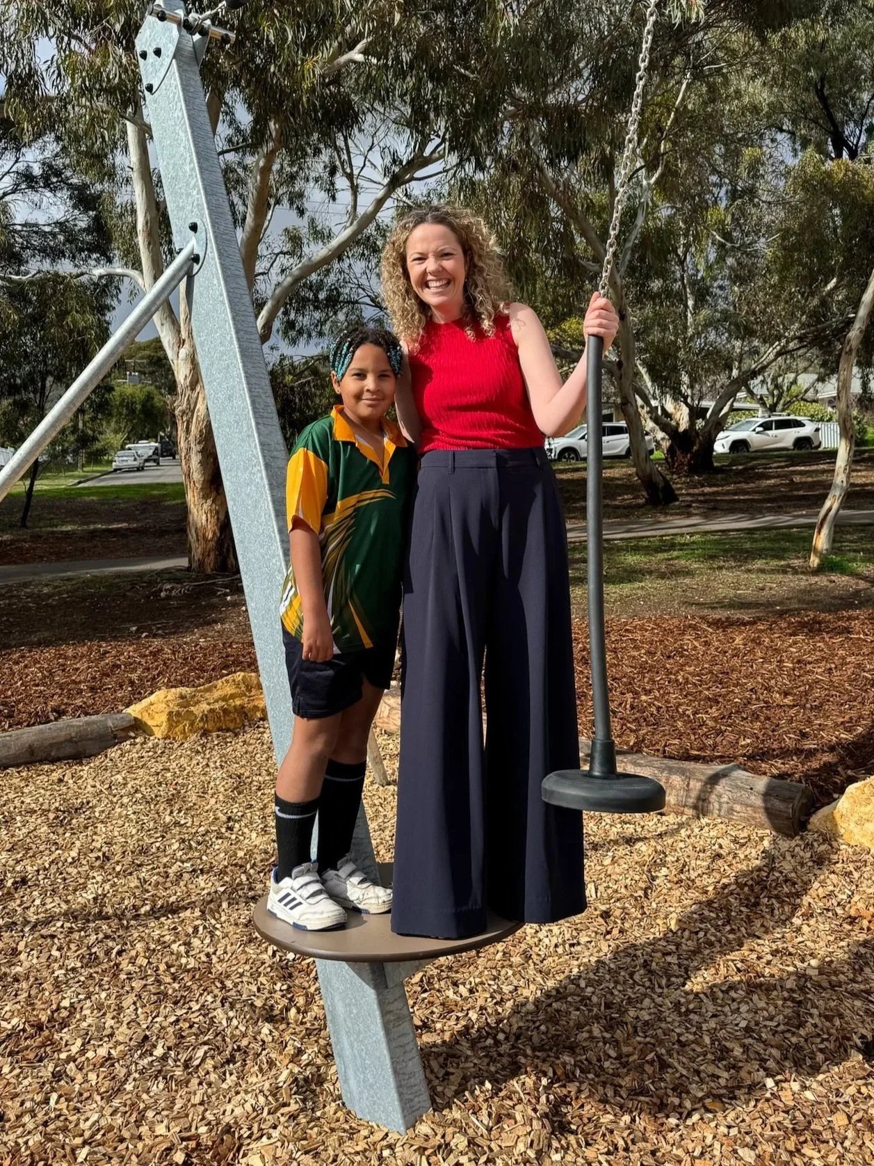 Nadia Clancy MP in a red top with navy trousers stood with a local child in school uniform on a zip line platform