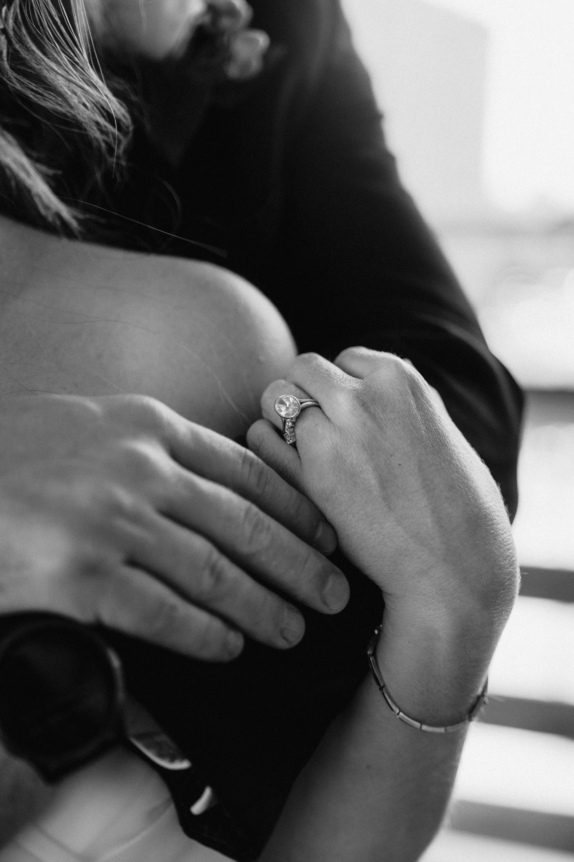 Close-up of a woman with a ring on her finger, resting her hand on a man's chest, in black and white.
