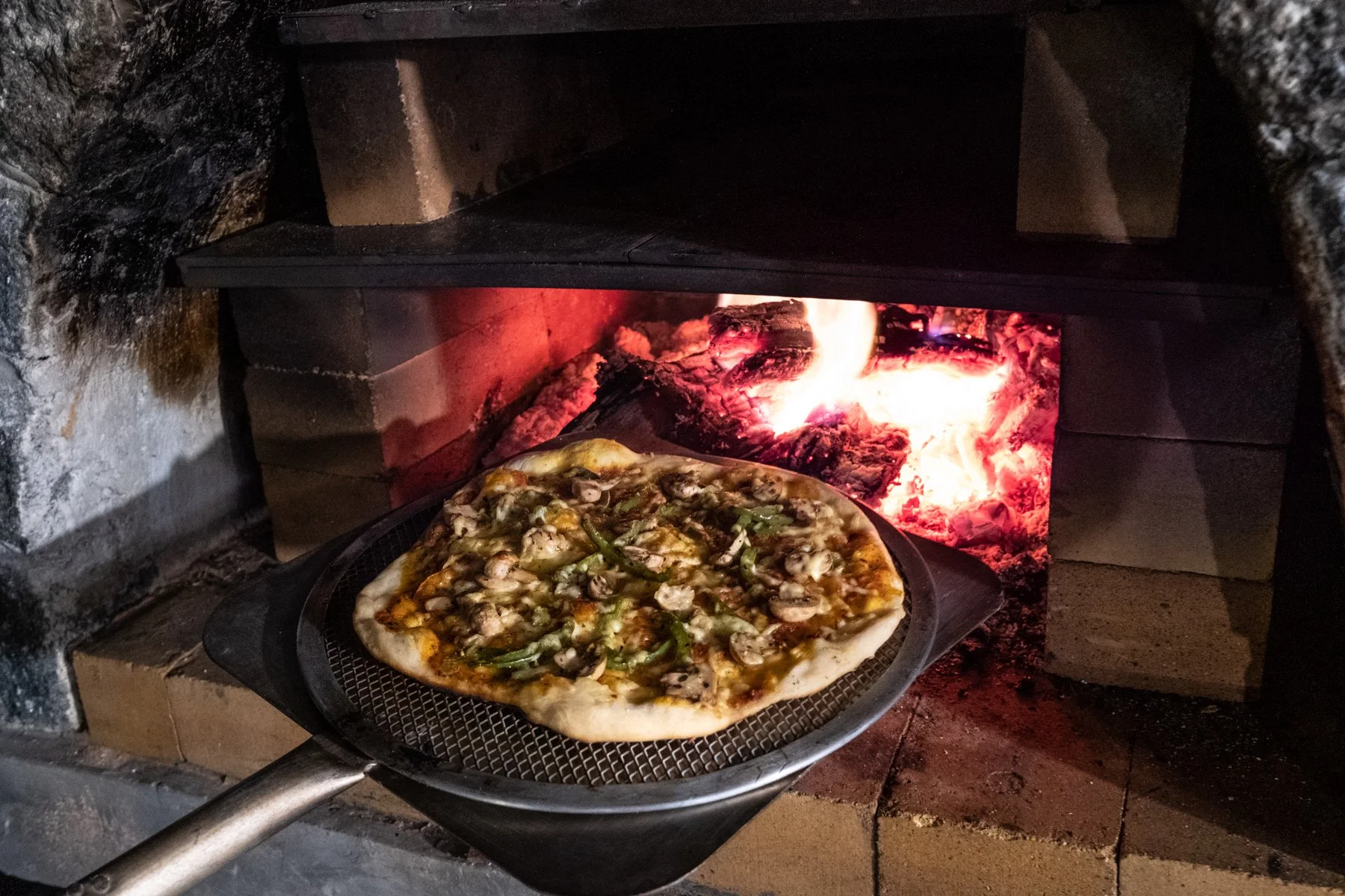 Pizza baking in a wood-fired oven with glowing embers inside.