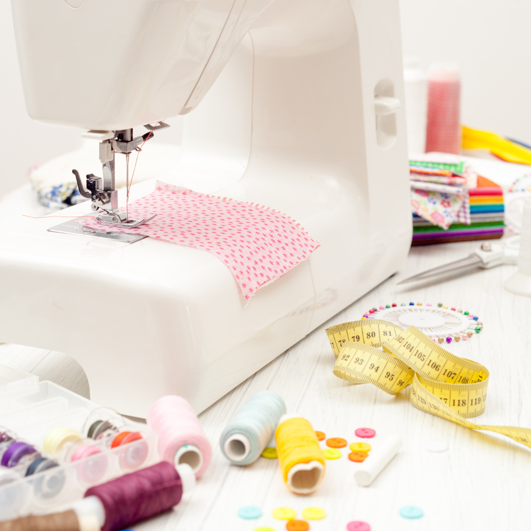 Sewing machine with pink fabric, colorful threads, measuring tape, and sewing supplies on a table.