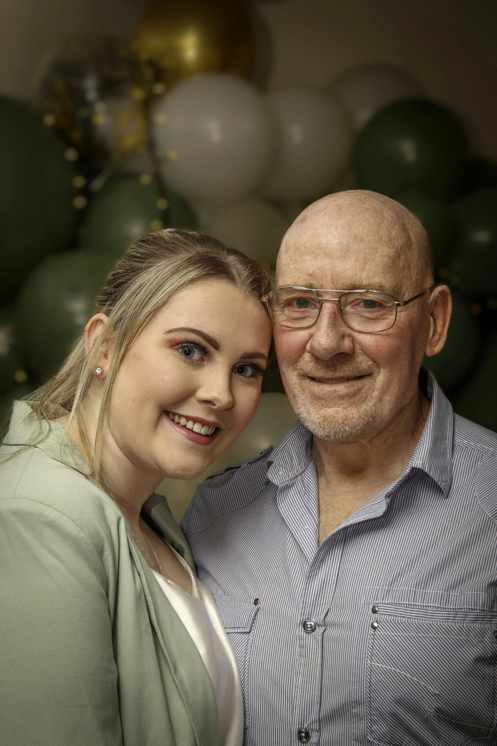 Close-up of a young woman and an older man smiling, with balloons in the background.
